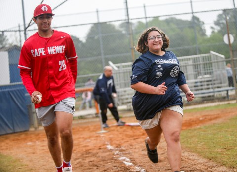 Trajan Taylor (20), left, runs to first base with his buddy Zoey Quintana, right, for a base hit during a Champions league game at the Great Neck Park in Virginia Beach, Virginia, on April 20, 2024. The Cape Henry Collegiate team, considered one of the top high school baseball teams in the state, plays a game every Saturday during the season, with one exception for their prom. The morning of their prom, they spend volunteering at the Champions league, a place designed to give special needs kids an opportunity to play baseball. "I think it's an awesome idea to come out and help the community and give back to some of the people that come watch our games and come support us, and just help grow the game of baseball to people who need a little bit extra help," Taylor said. (Billy Schuerman / APP)